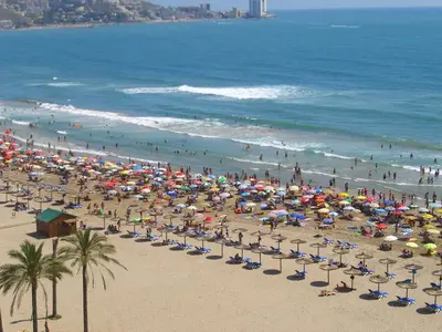 a beach with many chairs and umbrellas and people at Apartamento ÉLITE en Cullera playa San Antonio in Cullera