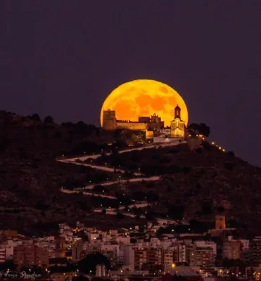 a large yellow moon rising over a city at night at Apartamento ÉLITE en Cullera playa San Antonio in Cullera