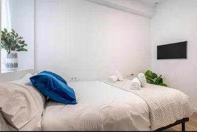 a white bedroom with a large bed with blue pillows at Lugre, Lovely flat close to center in Valencia