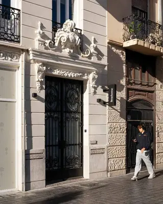 a man walking in front of a building with a door at Limehome Valencia de Xativa in Valencia