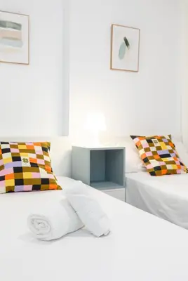 a white bedroom with two beds with colorful pillows at ApartUP Patacona Iconic I in Valencia