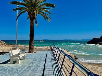 a boardwalk with two chairs and a palm tree on the beach at Faro Playa de Cullera in Faro de Cullera