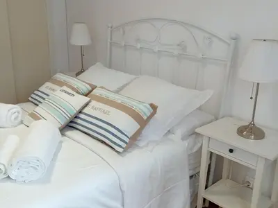 a white bed with white pillows and a night stand at Casa El Azud La Cañada 1 minuto metro in Partida de La Cañada