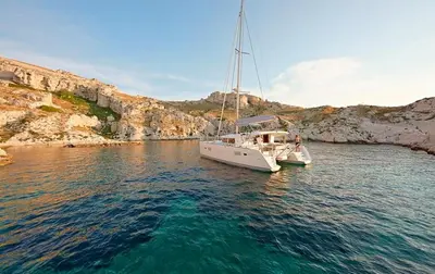 a white boat sitting in the water near a cliff at Catamaran Nora in Puebla de Farnals