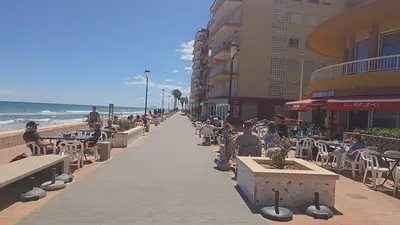 people sitting on benches on a sidewalk near the beach at Relax en familia junto al mar Les Palmeres in Sueca