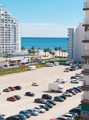 a parking lot with cars parked next to the beach at Marti, 7-38 in Cullera