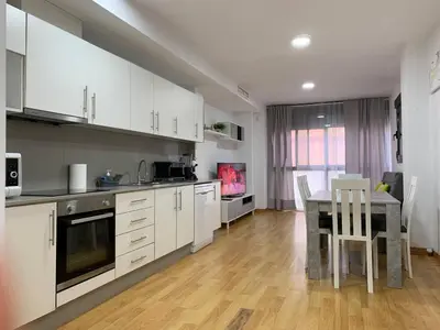 a kitchen with white cabinets and a table with chairs at Sunrise Beach Apartment Playa Puerto de Sagunto in Puerto de Sagunto