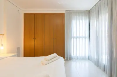 a bedroom with a white bed and a wooden cabinet at Apartamento con Vistas al mar, Piscina y Pista de Paddle in Valencia