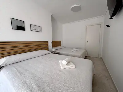a bedroom with two beds and a tv on the wall at VMC Rooms in Tavernes de Valldigna