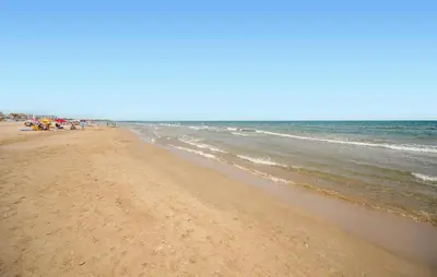 a beach with people standing on the sand and the water at Pet Friendly Home In Puerto De Sagunto in Puerto de Sagunto