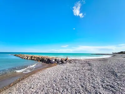 a person sitting on a rocky beach next to the ocean at Apartamento con terraza en Playa Grau de Moncofa in Moncófar