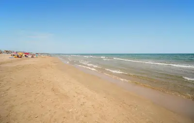 a beach with people standing on the sand and the water at Beach Front Apartment In Sagunto in Sagunto