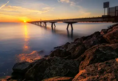 a bridge over the water at sunset with rocks at Au bord de la plage in Puerto de Sagunto