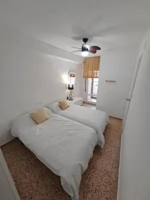 a bed in a white room with a ceiling fan at Au bord de la plage in Puerto de Sagunto