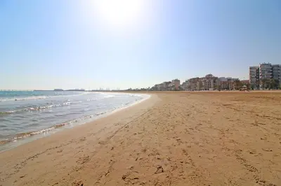 a sandy beach with buildings and the ocean at Global Vacacional, Apartamento con terraza en la playa de Puerto Sagunto in Puerto de Sagunto