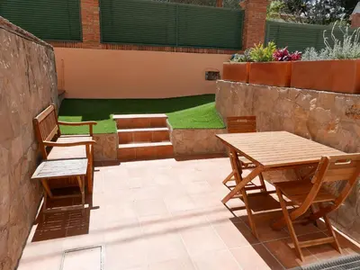 a patio with two wooden tables and chairs and a lawn at Natural park, terrace and pool in Partida de La Cañada