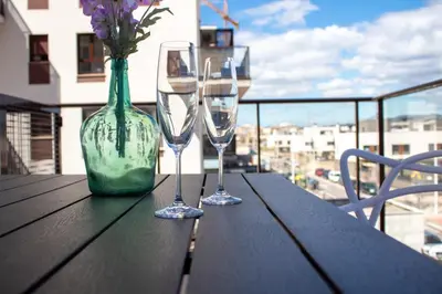 a table with two wine glasses and a vase with flowers at Global Vacacional, Apartamento con piscina en Puerto de Sagunto in Puerto de Sagunto