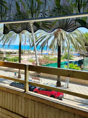 a red car driving down a road with palm trees at Avenida Mediterráneo in Puerto de Sagunto