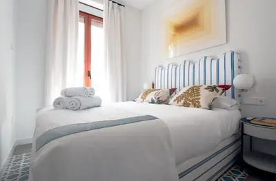 a white bedroom with a large white bed with blue accents at La Casa del Mar-Cabañal 3BR Suites in Valencia