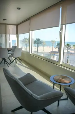 a room with a chair and a table and windows at Sucro Playa Apartment in Cullera