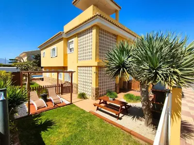 a yellow house with two chairs and a patio at VILLA ALGUER - Chalet junto a la playa del Marenyet de Cullera in Cullera