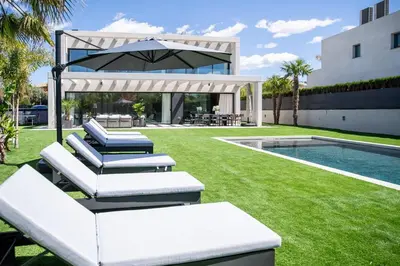 a lawn with lounge chairs and an umbrella next to a swimming pool at Villa Praya in Valencia in Bétera