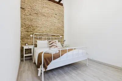 a white bed in a room with a brick wall at Hogar con encanto a 10 min del centro de Valencia in Valencia