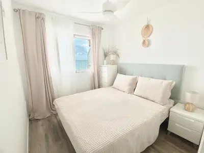 a white bedroom with a bed and a window at Beach Apartment in Cullera