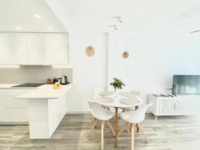 a white kitchen with a table and white chairs at Beach Apartment in Cullera