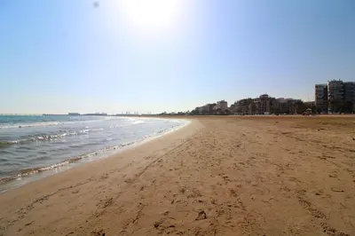 a beach with the ocean and buildings in the background at Global Vacacional, Bonito apartamento cerca de la playa in Puerto de Sagunto