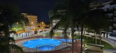 a swimming pool with palm trees and a building at Apartamento Timia OASIS in Canet de Berenguer