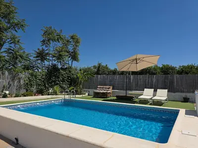 a swimming pool with an umbrella and two chairs and a couch at Villa Entre-Azahar, Tu refugio de tranquilidad in Lliria