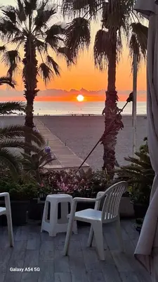 a sunset on the beach with palm trees and chairs at Apartamento con gran terraza frente al Mar playa Valencia in Valencia