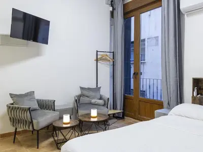 a bedroom with a bed and two chairs and a tv at Winahost Loft Colón in downtown Valencia in Valencia