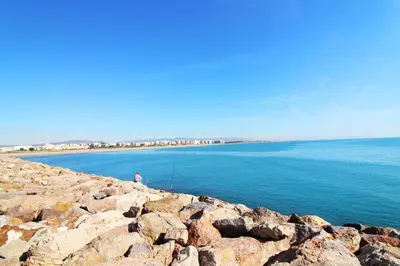 a person sitting on a rocky shoreline with the ocean at Global Vacacional, Apartamento con gran terraza en la playa de Puerto Sagunto in Puerto de Sagunto
