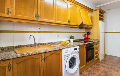 a kitchen with wooden cabinets and a washing machine at MoYma Playa in Puerto de Sagunto