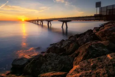 a bridge over the water at sunset with rocks at MoYma Playa in Puerto de Sagunto