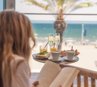 a woman sitting at a table with food and drinks at Meraki Beach Hotel - Only Adults in Playa Pobla de Farnals