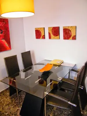 a glass table with chairs and paintings on the wall at Apartamentos Milenio in Cullera