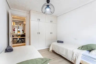 a white bedroom with two beds and a chandelier at Big apartment at beach with terrace in Valencia