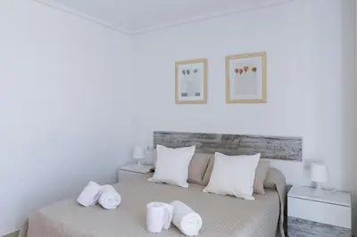 a white bedroom with a bed with towels on it at ApartUP Patacona Horizon in Valencia