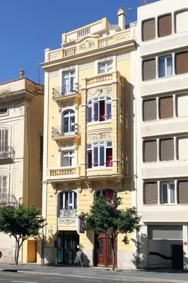 a tall yellow building with windows on a street at Purple Nest Hostel in Valencia