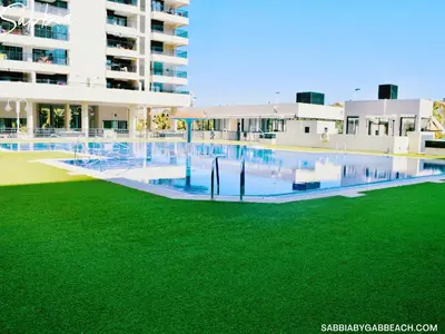 a swimming pool with green grass in front of a building at Sabbia Valencia Apartment in Valencia