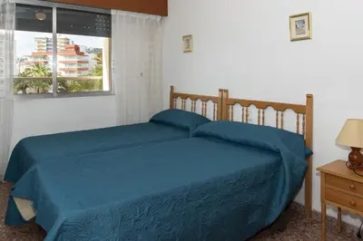 a bedroom with a bed with blue sheets and a window at Florazar 2, Vi-3-B in Faro de Cullera
