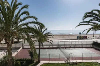 a tennis court with palm trees and the beach at Lider, 2-I in Cullera