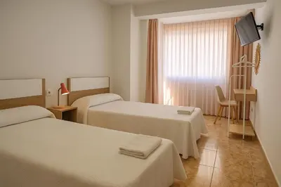 a hotel room with two beds and a television at Rooms Avenida in Tavernes de Valldigna