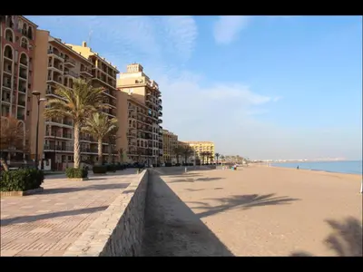 a beach with buildings and palm trees next to the ocean at Cozy apartment on the sea in Port Saplaya