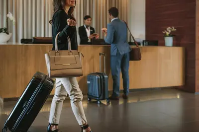 a woman walking with a suitcase and a man standing behind a counter at Hotel Vila-real Palace in Villareal