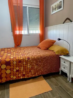 a bedroom with a bed with an orange curtain and a window at Apt. New Holiday Valencia Beach in El Puig