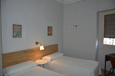 a room with two beds and a table and a window at Pensión Moratin in Valencia